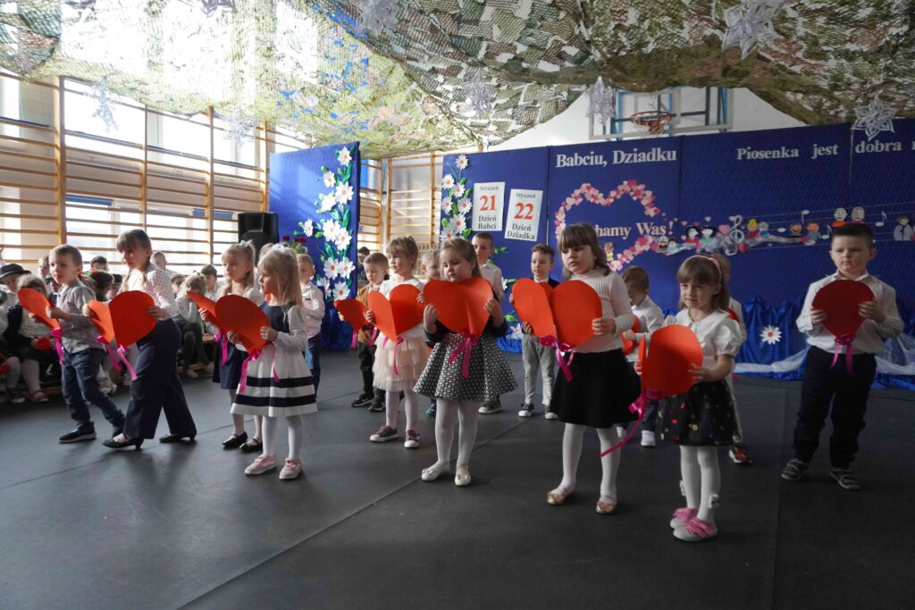 Dzieci tańczą, w dłoniach trzymają papierowe czerwone serca.