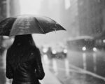 kobieta stoi w deszczu, w ręku trzyma parasol