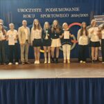 Grupa osób pozuje do zdjęcia podczas uroczystości zakończenia roku sportowego. W centrum znajdują się nagrodzeni zawodnicy trzymający dyplomy, medale lub puchary.