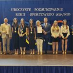 Grupa osób pozuje do zdjęcia podczas uroczystości zakończenia roku sportowego. W centrum znajdują się nagrodzeni zawodnicy trzymający dyplomy, medale lub puchary.