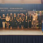 Grupa osób pozuje do zdjęcia podczas uroczystości zakończenia roku sportowego. W centrum znajdują się nagrodzeni zawodnicy trzymający dyplomy, medale lub puchary.