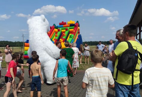 Zdjęcie przedstawia grupę dzieci, bawiących się na dmuchańcach i z maskotką niedźwiedzia, podczas pikniki w Zdziwóju.