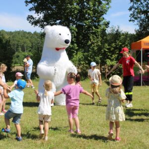 Animacje dla dzieci. Dzieci stoją wokół wielkiej maskotki białego niedźwiedzia. W tle stoiska piknikowe.