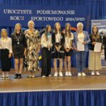 Grupa osób pozuje do zdjęcia podczas uroczystości zakończenia roku sportowego. W centrum znajdują się nagrodzeni zawodnicy trzymający dyplomy, medale lub puchary.