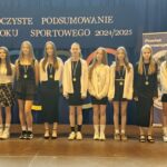Grupa osób pozuje do zdjęcia podczas uroczystości zakończenia roku sportowego. W centrum znajdują się nagrodzeni zawodnicy trzymający dyplomy, medale lub puchary.