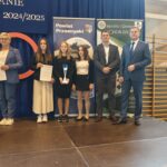 Grupa osób pozuje do zdjęcia podczas uroczystości zakończenia roku sportowego. W centrum znajdują się nagrodzeni zawodnicy trzymający dyplomy, medale lub puchary.