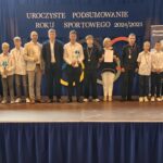 Grupa osób pozuje do zdjęcia podczas uroczystości zakończenia roku sportowego. W centrum znajdują się nagrodzeni zawodnicy trzymający dyplomy, medale lub puchary.