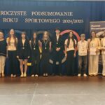 Grupa osób pozuje do zdjęcia podczas uroczystości zakończenia roku sportowego. W centrum znajdują się nagrodzeni zawodnicy trzymający dyplomy, medale lub puchary.