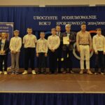 Grupa osób pozuje do zdjęcia podczas uroczystości zakończenia roku sportowego. W centrum znajdują się nagrodzeni zawodnicy trzymający dyplomy, medale lub puchary.