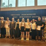 Grupa osób pozuje do zdjęcia podczas uroczystości zakończenia roku sportowego. W centrum znajdują się nagrodzeni zawodnicy trzymający dyplomy, medale lub puchary.