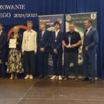 Grupa osób pozuje do zdjęcia podczas uroczystości zakończenia roku sportowego. W centrum znajdują się nagrodzeni zawodnicy trzymający dyplomy, medale lub puchary.