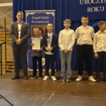 Grupa osób pozuje do zdjęcia podczas uroczystości zakończenia roku sportowego. W centrum znajdują się nagrodzeni zawodnicy trzymający dyplomy, medale lub puchary.