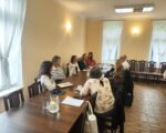 Grupa ludzi siedzi przy duży stole konferencyjnym.