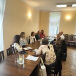 Grupa ludzi siedzi przy duży stole konferencyjnym.