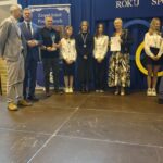 Grupa osób pozuje do zdjęcia podczas uroczystości zakończenia roku sportowego. W centrum znajdują się nagrodzeni zawodnicy trzymający dyplomy, medale lub puchary.