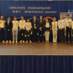 Grupa osób pozuje do zdjęcia podczas uroczystości zakończenia roku sportowego. W centrum znajdują się nagrodzeni zawodnicy trzymający dyplomy, medale lub puchary.