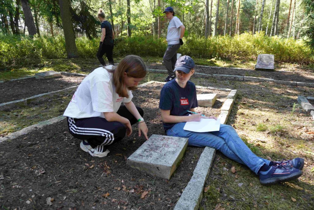 Dwie dziewczyny siedzą przy tablicy wojennej i odczytują napis na tablicy.