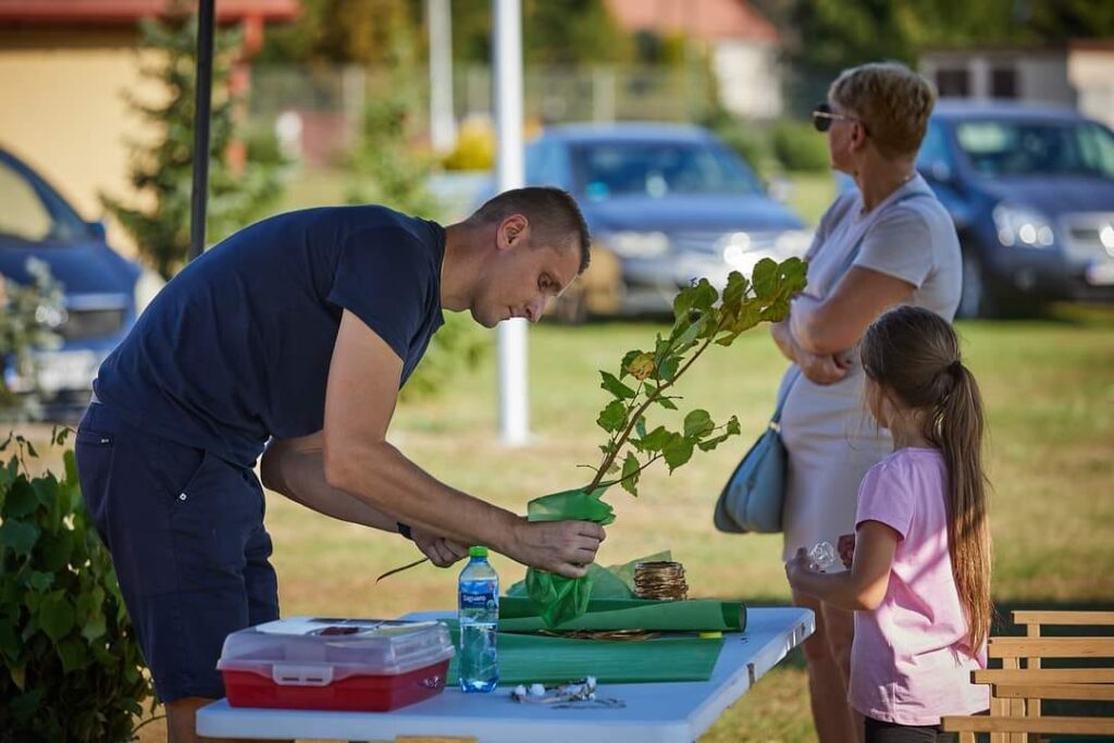 Mężczyzna trzyma sadzonkę drzewka, obok stoi kobieta i dziewczynka.