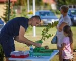 Mężczyzna trzyma sadzonkę drzewka, obok stoi kobieta i dziewczynka.