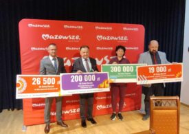 Na zdjęciu widoczni są przedstawiciele Województwa Mazowieckiego oraz gminy Chorzele podczas uroczystego wręczenia dofinansowania. Czterech uczestników uroczystości - trzech mężczyzn i jedna kobieta - pozuje do zdjęcia, trzymając w rękach cztery duże symboliczne czeki. Na każdym z czeków widnieje kwota dofinansowania oraz nazwa zadania, które otrzymało wsparcie finansowe. Osoby ustawione są obok siebie w jednym rzędzie.